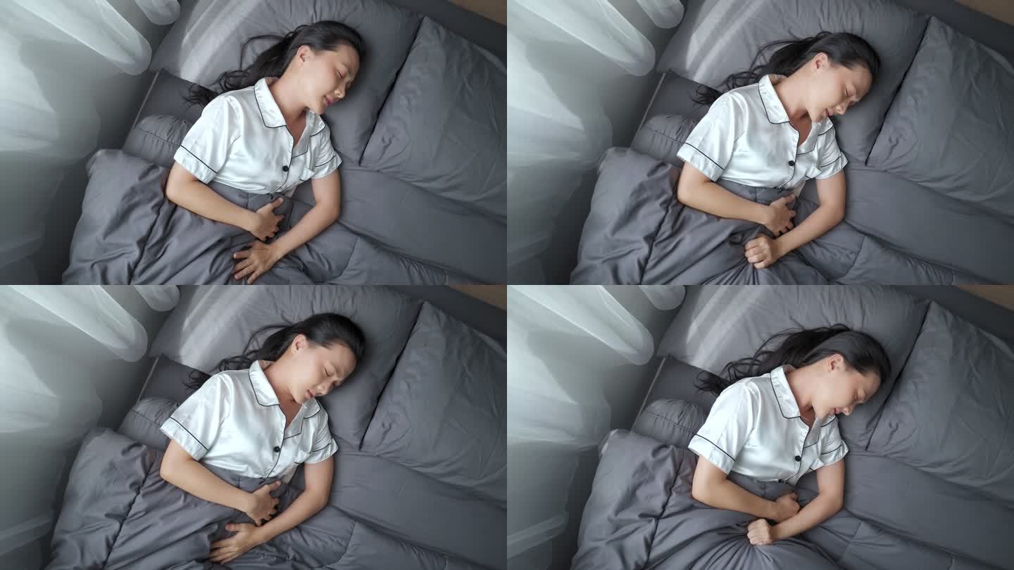 早上躺在床上的一位亚洲妇女胃痛。俯视图。