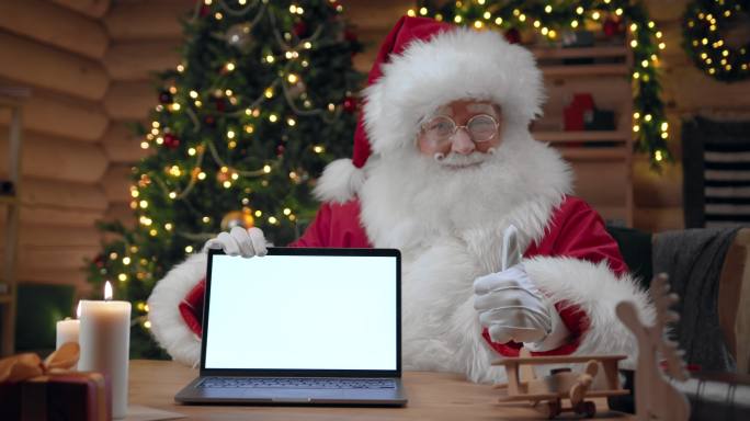 圣诞老人打开一台空白屏幕的笔记本电脑，在相机中竖起大拇指