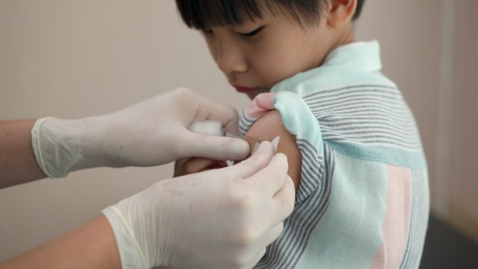 男医生在接种疫苗后给男孩的手臂缠上绷带。