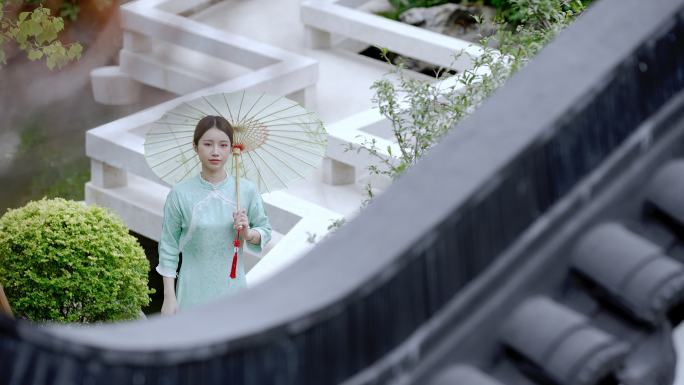 年轻旗袍女子打着纸伞走过中式合院观景桥