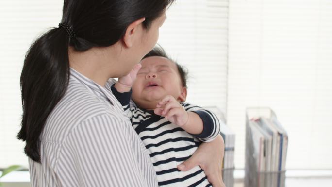 年轻的亚洲母亲抱着哭泣的新生儿，安慰着她。
