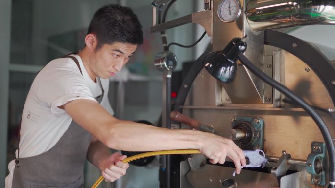 亚裔中国工人，带手套吹洗和清洁咖啡烘焙机，带真空清洁鼓风机