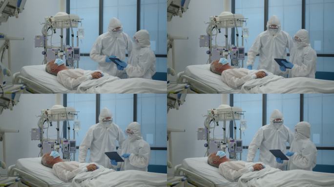 在新冠肺炎大流行期间，一组佩戴PPE的医生在ICU检查一名患者，查看平板电脑上的病历