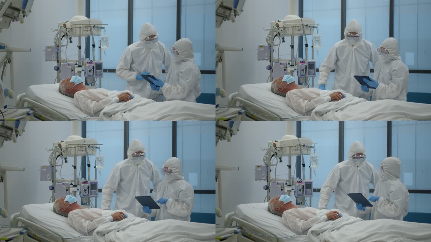 在新冠肺炎大流行期间，一组佩戴PPE的医生在ICU检查一名患者，查看平板电脑上的病历