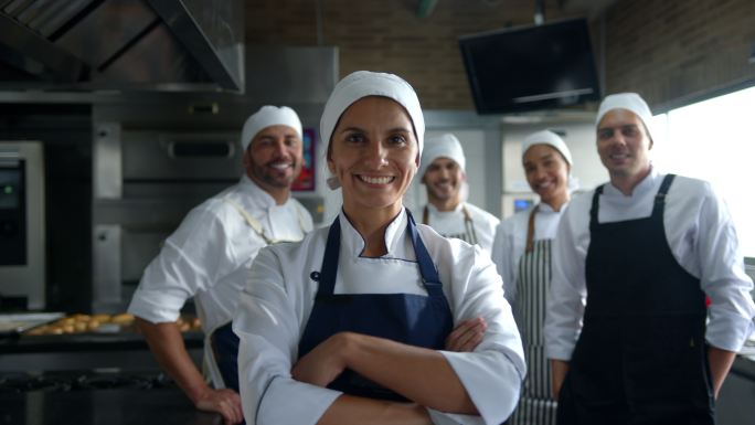 一群快乐的拉丁美洲面包师在一家面包店工作，面带微笑面对镜头，女领导交叉双臂站在前台