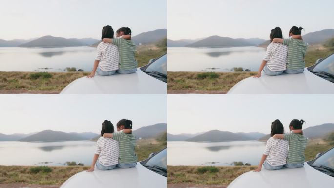 亚洲兄弟姐妹小女孩坐在车上，一起玩耍，在风景优美的大坝公园享受假期野餐。快乐家庭汽车旅行理念。
