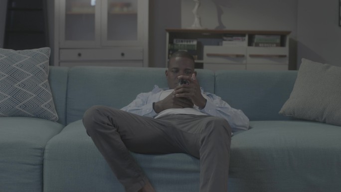 非州男人坐在沙发上玩手机视频聊天葛优躺