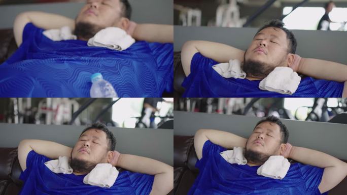 特写镜头，一个非常胖的家伙在健身房健身课结束后，睡在沙发上，把水瓶靠在肚子上。