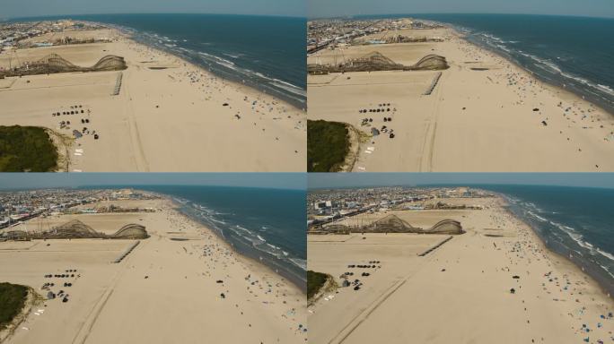 阳光明媚的一天，新泽西州泽西海岸威德伍德的沙滩上，有着过山车和其他景点的游乐园。部分轨道宽平移摄像机