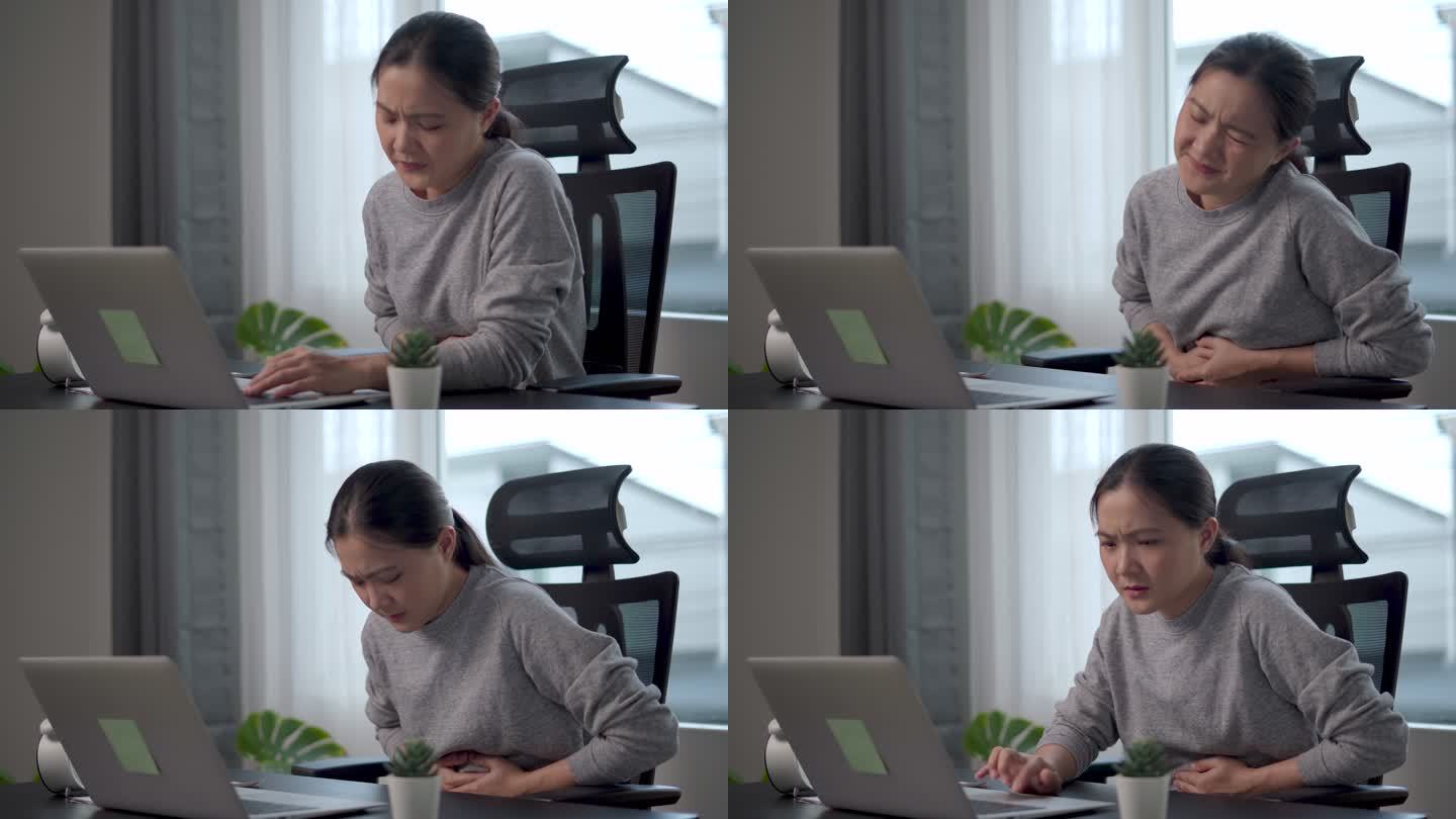 一位亚洲女性坐在家里的办公室里，胃疼得很厉害。