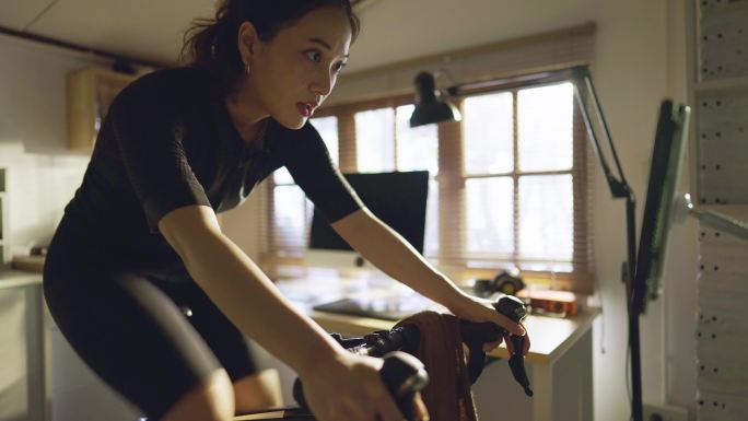 亚洲女自行车手，她正在家里锻炼。她骑自行车模拟器。