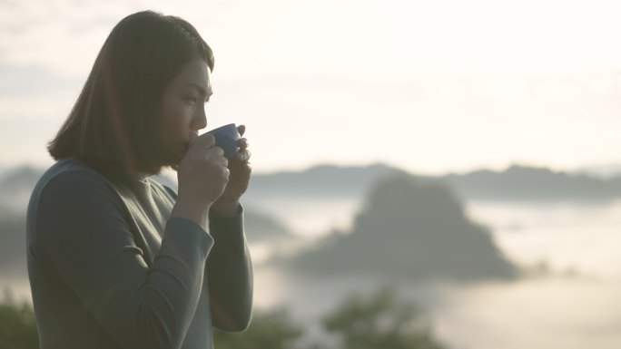 早上，女人在山上用咖啡杯在户外放松