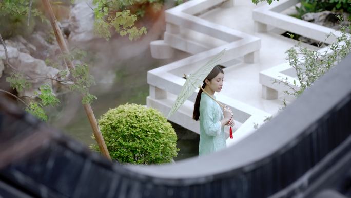 年轻旗袍女子打着纸伞走过中式合院观景桥