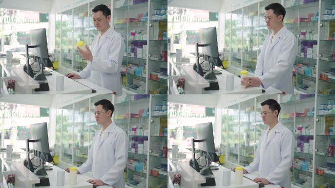 自信的亚洲男性药剂师，在药房药店的台式计算机数据库上执行微笑管理任务。医学、药剂学、保健与人的观念
