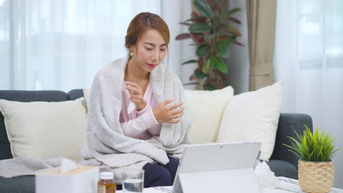 亚洲年轻女性躺在沙发上，与家里平板电脑上的医生进行视频会议