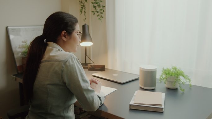 智能扬声器数字助理技术。在笔记本电脑上工作时，女性提问语音激活了智能扬声器设备。自动提醒并获得日常任