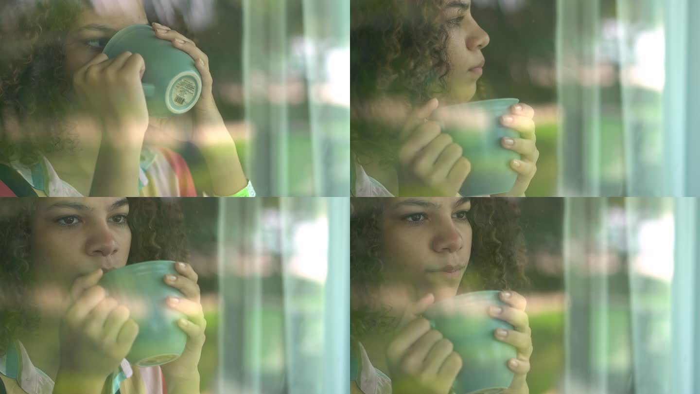 年轻女子在阳台门玻璃后面喝咖啡