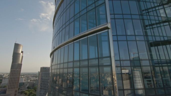 反射蓝天的玻璃摩天大楼。FPV无人机在大楼内快速转弯