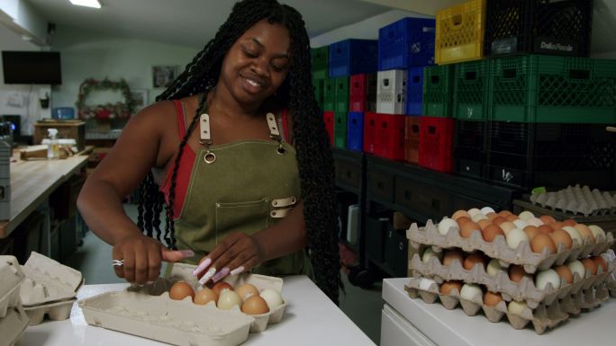 科罗拉多州当地一家小型商业农场，一位快乐的非裔美国妇女，长着时尚的指甲，正在打包新鲜的农场鸡蛋，准备