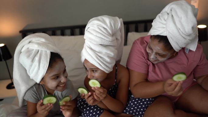 躺在床上用黄瓜片遮住眼睛进行皮肤护理的母亲和女儿