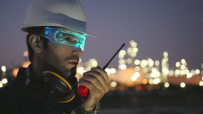 戴着高科技人工智能眼镜或虚拟现实眼镜的白人或中东工程师检查炼油厂的状况并使用对讲机。