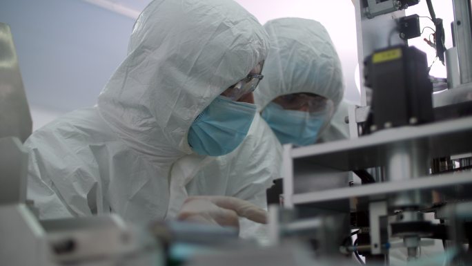 两个研究医用口罩工厂洁净室、工程师和科学家穿着罩衣与数字平板电脑交谈