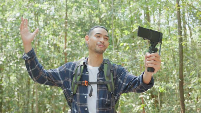亚洲帅气的男性背包客vlogger独自在森林里旅行。迷人的男旅行者在假期旅行中使用手机记录视频日志，