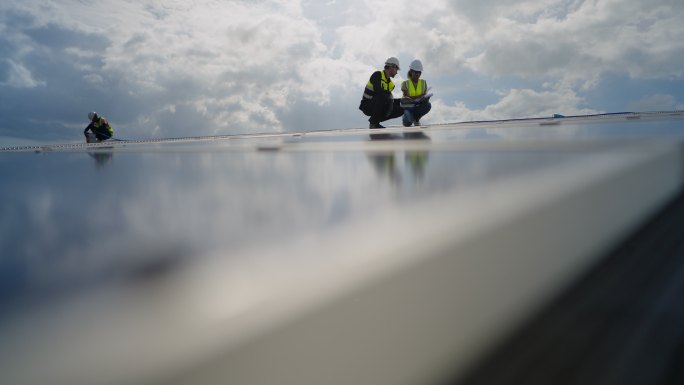 男工业工程师和女技术人员穿着安全制服在屋顶工厂工作，检查维护和修理太阳能电池板。可再生能源工业。太阳