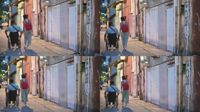后视坐轮椅的亚裔中国游客晚上在城市街道与女朋友聊天