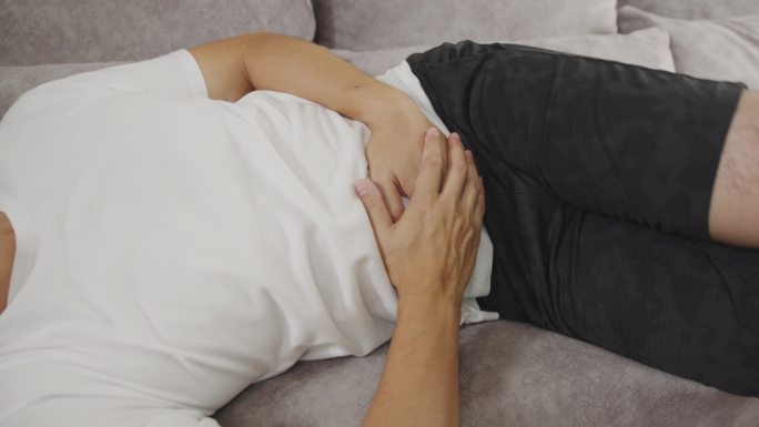一名亚洲男子躺在沙发上，在家中胃痛