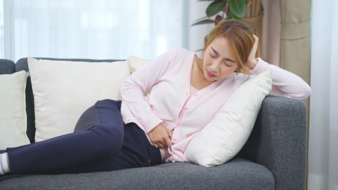 亚洲女性胃痛，躺在家里的沙发上。经期疼痛