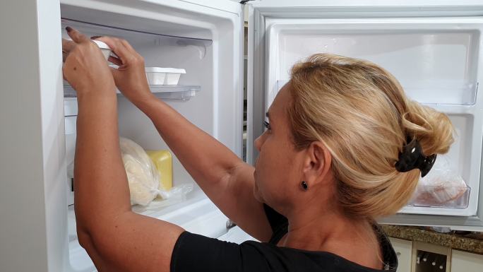 家庭主妇把冰块托盘放在冰箱里