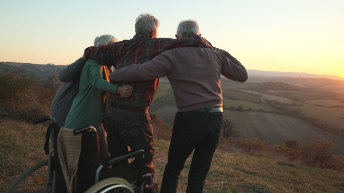 一群老年人帮助他们的残疾朋友和他们一起站着欣赏风景。