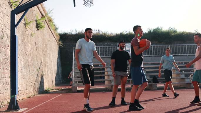 在一个温暖的春天，一群运动员朋友在户外球场上享受篮球比赛。