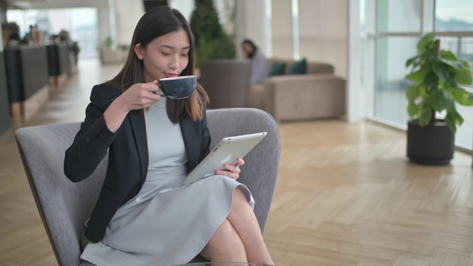 一位亚洲中国美女在贵宾休息室一边享用咖啡，一边使用数字平板电脑上网