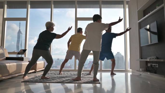 一位亚裔中国老人晚上在公寓起居室里教他的老朋友打太极，享受家庭锻炼