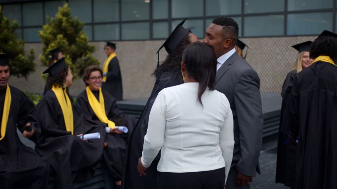 毕业典礼后，一位美丽的黑人妇女与同学交谈，然后兴奋地问候她的父母