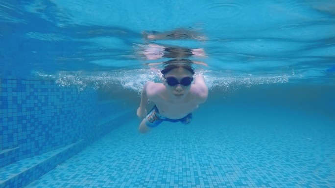 假期中，低角度观看亚裔中国少年游泳穿过游泳池。