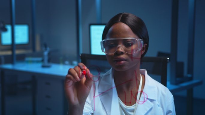 一位年轻的黑皮肤科学家身穿白色实验服，在现代实验室的玻璃板上写下化学公式，然后戴上防护眼镜，微笑着看