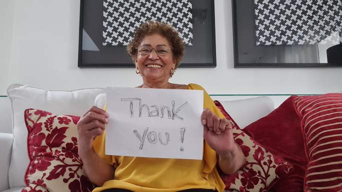 在视频通话中展示写有“谢谢”的纸的资深女性-网络摄像头视角