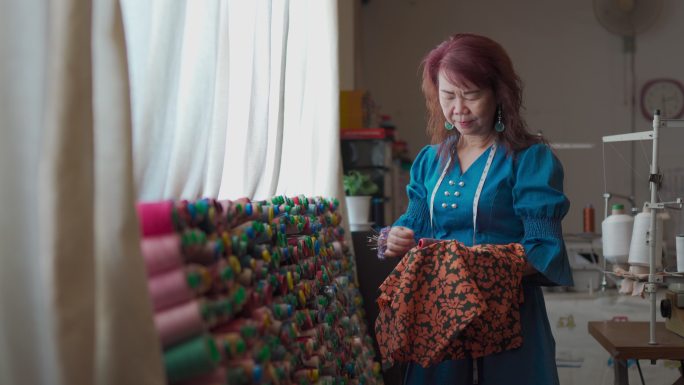 亚裔中国高级女裁缝在工作室挑选配线面料服装