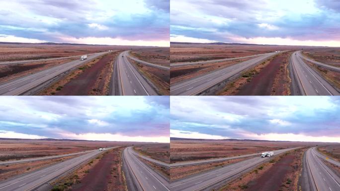黄昏或黎明时在荒凉沙漠中四车道公路上行驶的长途货运半卡车和拖车