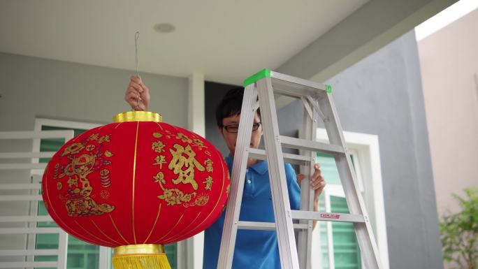 除夕夜，一名亚洲中国男子在家前院挂红灯笼