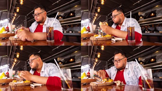 胖子年轻人在服务员端汉堡包之前使用手机的情景。男人在快餐店饥肠辘辘地吃汉堡包。