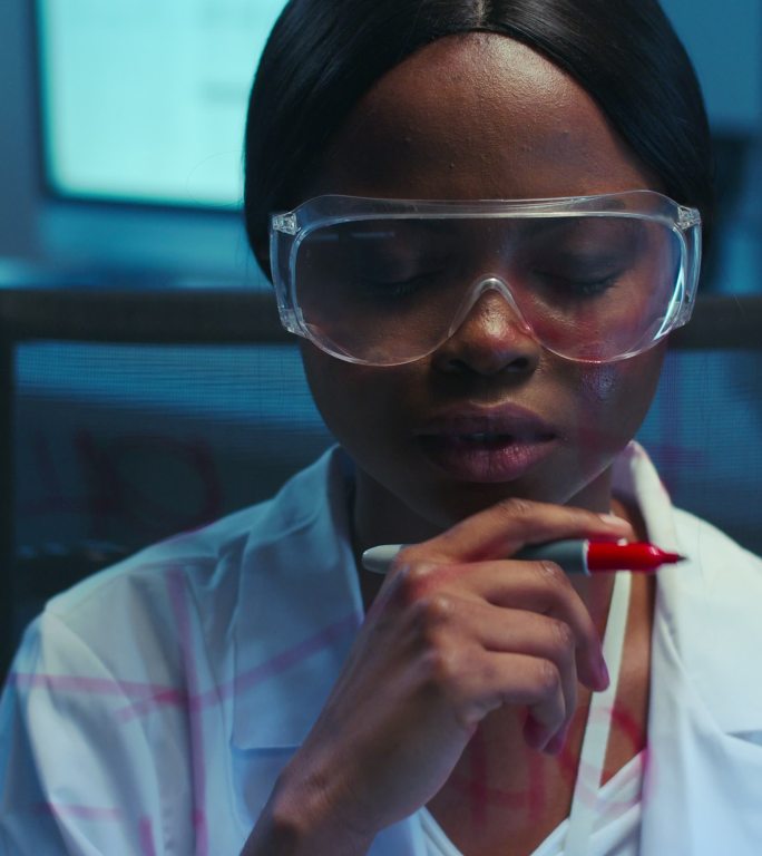 一位年轻、有思想的非洲裔美国科学家在现代实验室的前景玻璃板上写化学公式
