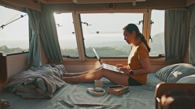 在房车露营期间，年轻的亚洲女性在卧室里用笔记本电脑放松，然后进行远程工作。