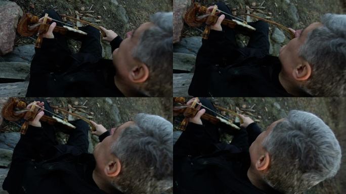 男人在树前的石墙旁拉小提琴。Gusle库存视频