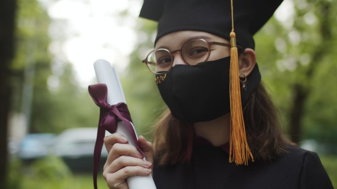 十几岁的女孩穿着毕业礼服和帽子，戴着防护口罩