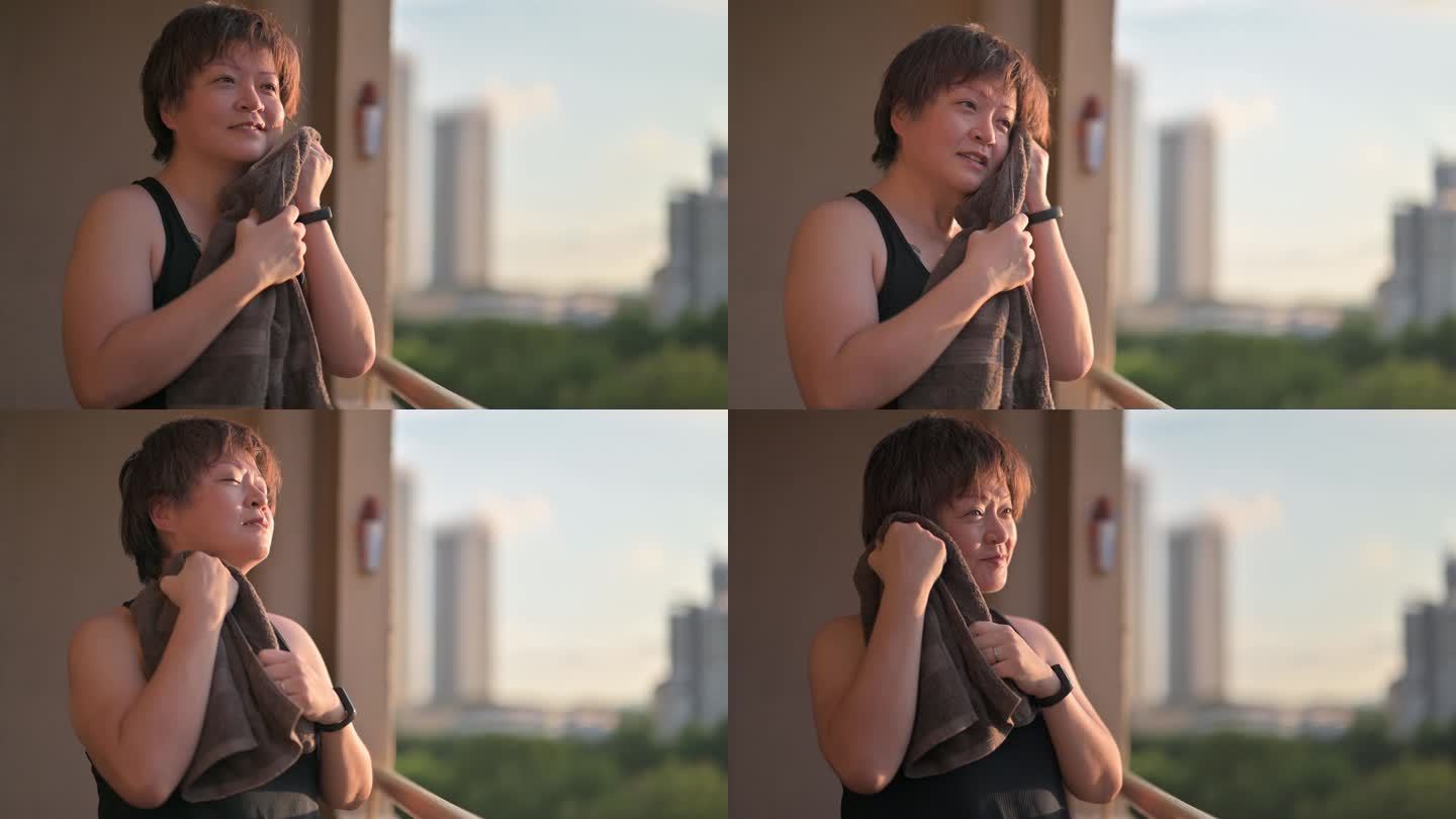早上锻炼后，亚洲中国中年女性微笑着看着阳台，休息时用干净毛巾擦汗