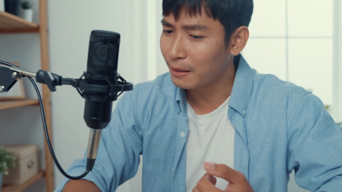 这张特写镜头是一位亚洲年轻男子用显微镜在家里客厅的工作台上用笔记本电脑录制播客。